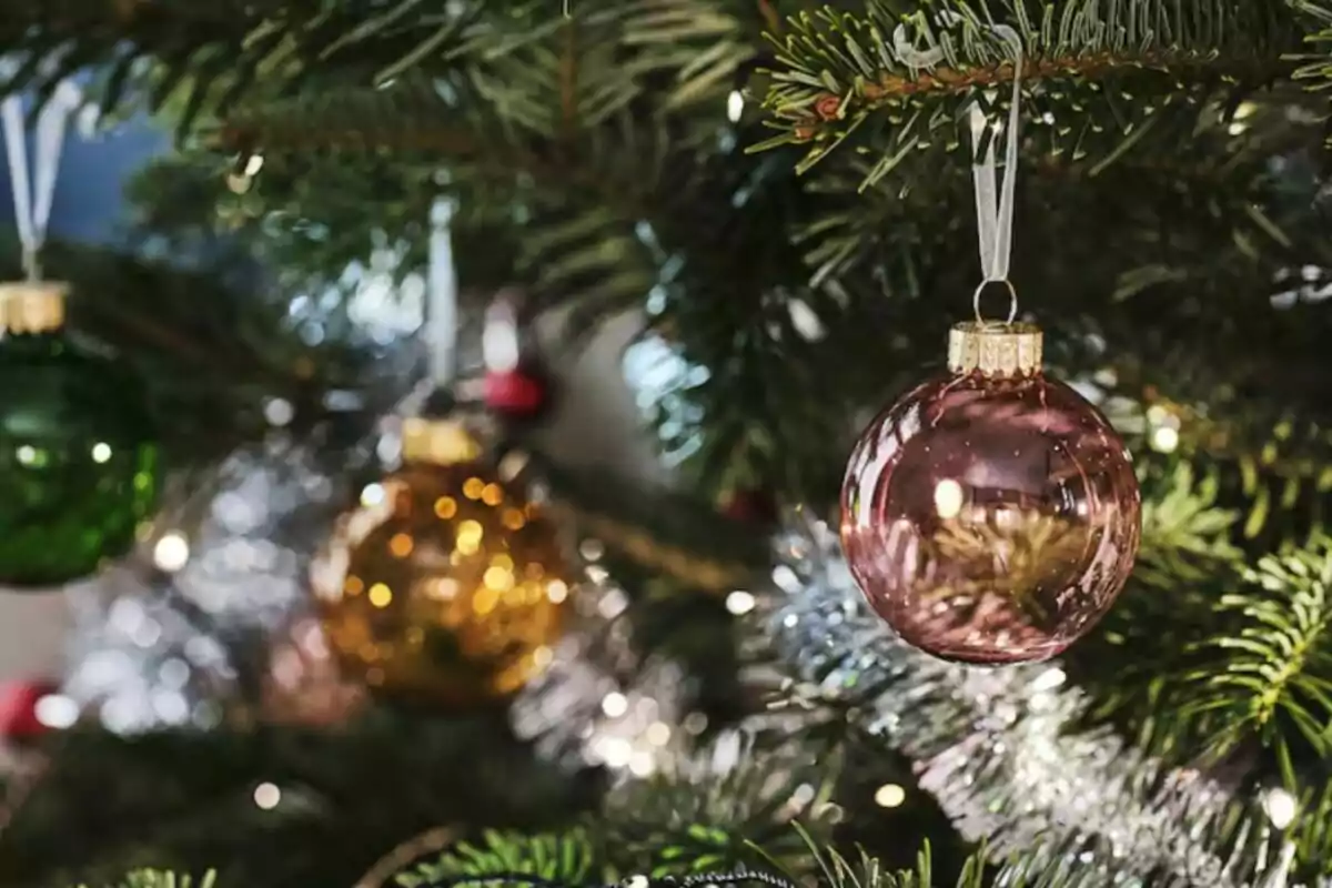 Adornos navideños colgando de un árbol de Navidad con luces brillantes.