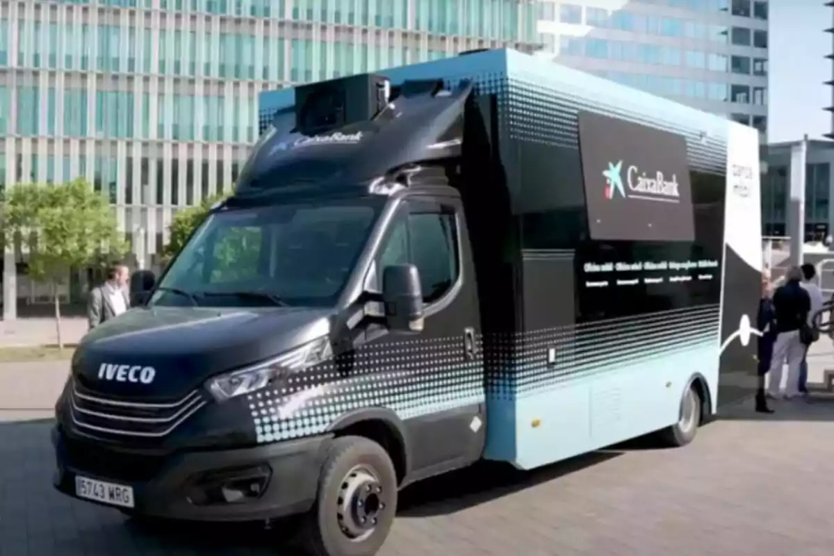 Camió d'Iveco amb logotip de CaixaBank estacionat a una zona urbana amb edificis moderns de fons.