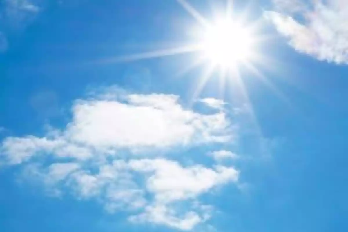 Cielo azul con nubes esponjosas y el sol brillando intensamente.
