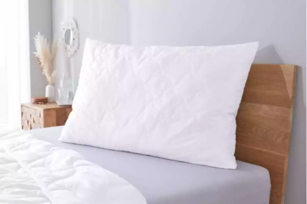 Coixí blanc sobre un llit amb capçal de fusta en una habitació decorada amb tons clars Coixí blanc sobre un llit amb capçal de fusta en una habitació decorada amb tons clars