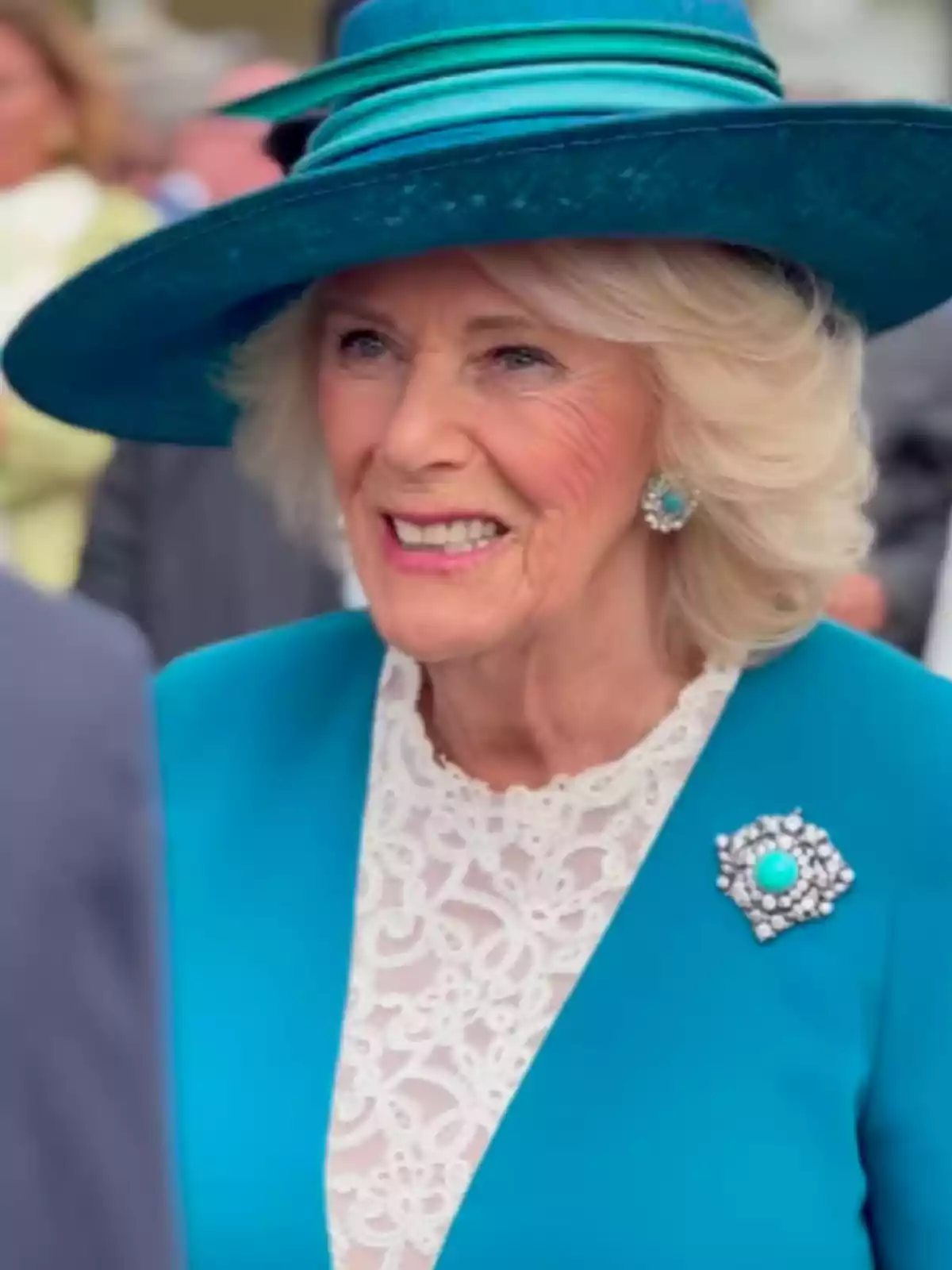 A smiling woman with a blue hat and a matching brooch in her elegant outfit. A smiling woman with a blue hat and a matching brooch in her elegant outfit.