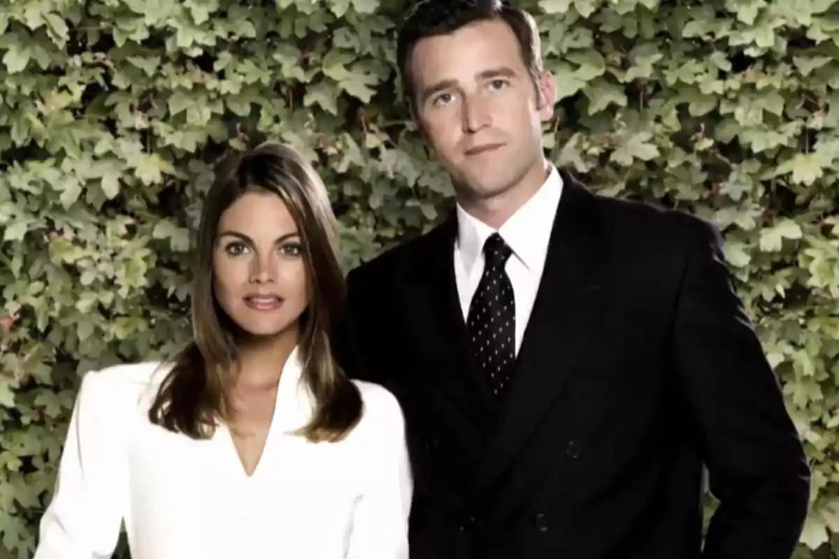 Amaia Salamanca in a white blazer and Fernando Gil in a dark suit pose together in front of a backdrop of green leaves. Amaia Salamanca in a white blazer and Fernando Gil in a dark suit pose together in front of a backdrop of green leaves.