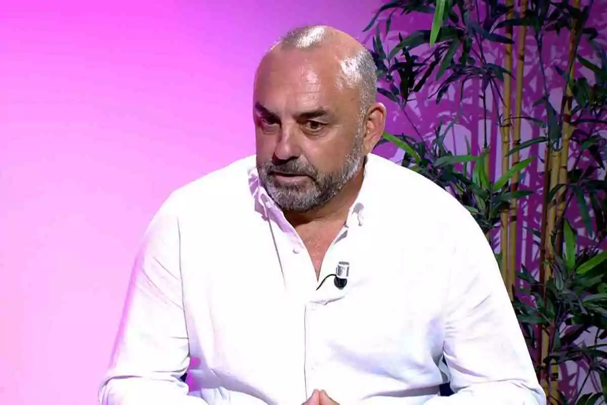 Ginés Corregüela amb barba i camisa blanca assegut davant d'un fons rosa amb plantes.