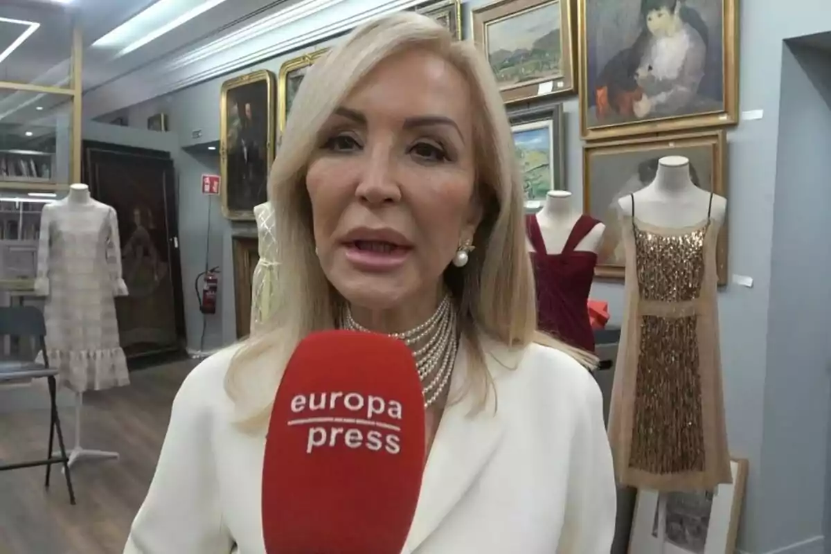 Carmen Lomana sosté un micròfon d'Europa Press en un entorn amb maniquins i quadres a la paret.