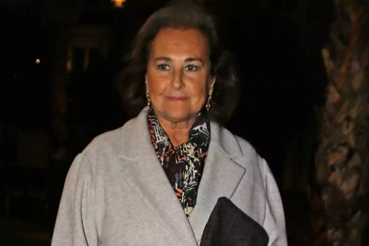 Carmen Tello, vestida amb un abric gris i una bufanda estampada, sosté una bossa negra mentre somriu lleugerament en un entorn fosc. Carmen Tello, vestida amb un abric gris i una bufanda estampada, sosté una bossa negra mentre somriu lleugerament en un entorn fosc.