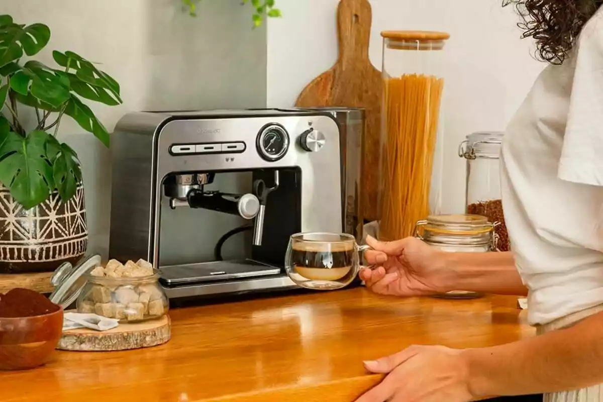 Persona preparant cafè amb una màquina d'espresso en una cuina, envoltada de plantes i pots d'ingredients.