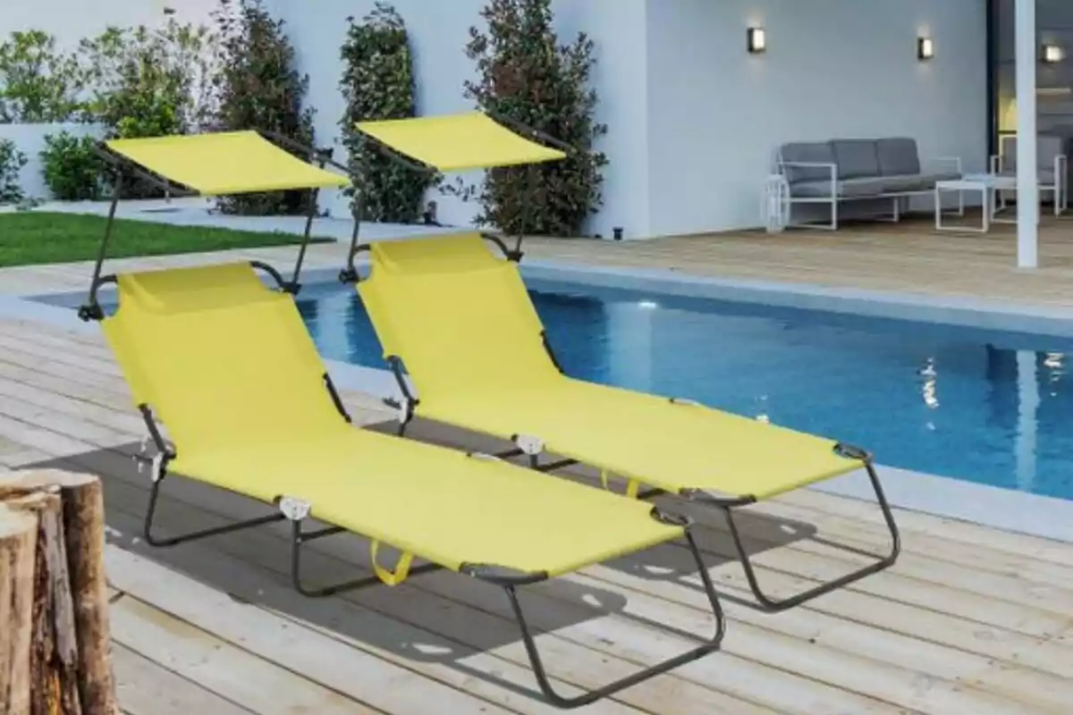 Dues gandules grogues amb tendal al costat d’una piscina en una terrassa de fusta Dues gandules grogues amb tendal al costat d’una piscina en una terrassa de fusta