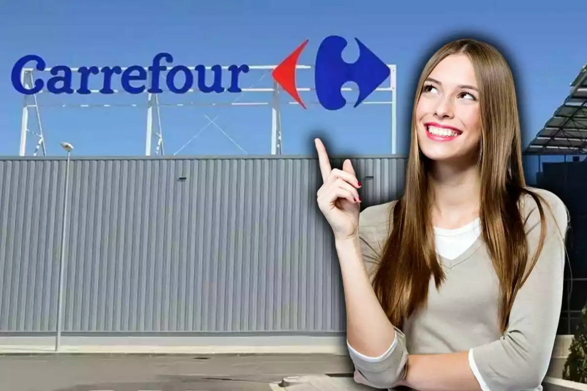 Dona somrient assenyalant cap al rètol de Carrefour a la façana d’un edifici sota un cel serè