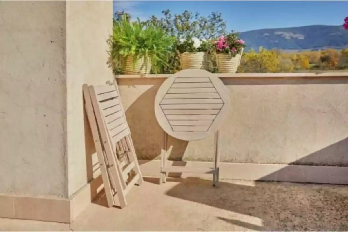 Cadires i taula plegables de fusta recolzades en una paret de terrassa amb testos i vista a les muntanyes al fons Cadires i taula plegables de fusta recolzades en una paret de terrassa amb testos i vista a les muntanyes al fons
