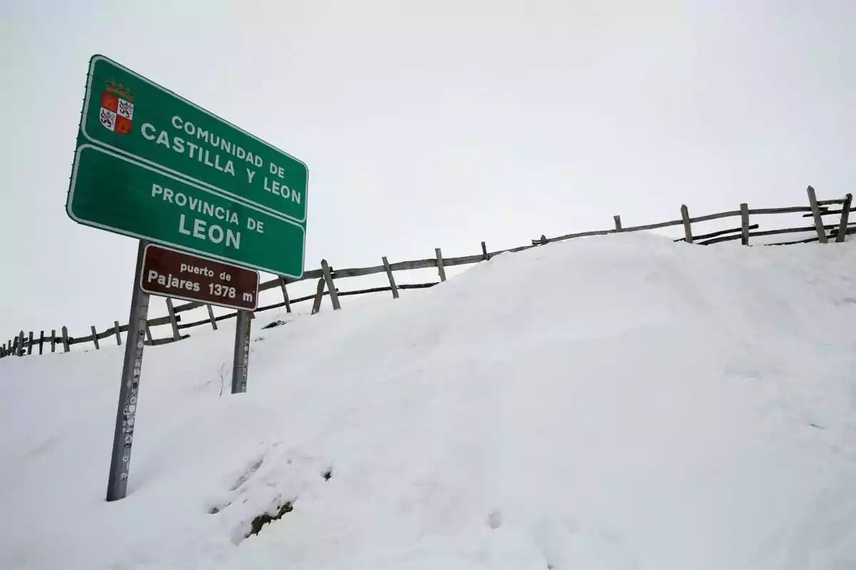 Un cartel verde indica la entrada a la Comunidad de Castilla y León y la Provincia de León en el puerto de Pajares a 1378 metros de altitud rodeado de nieve y una cerca de madera.