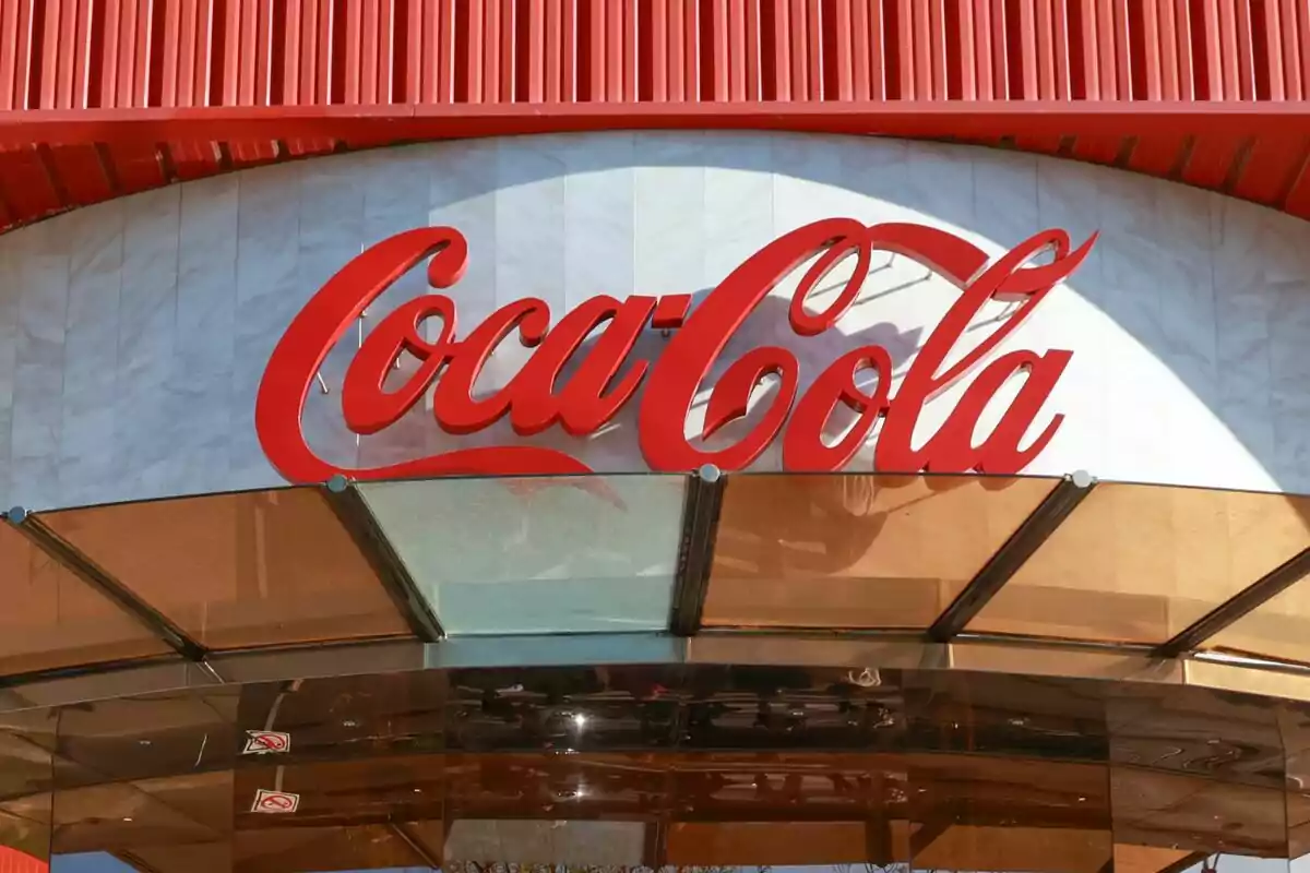 Entrada d'un edifici amb el logotip de Coca-Cola en lletres vermelles sobre un fons blanc i estructura de vidre. Entrada d'un edifici amb el logotip de Coca-Cola en lletres vermelles sobre un fons blanc i estructura de vidre.