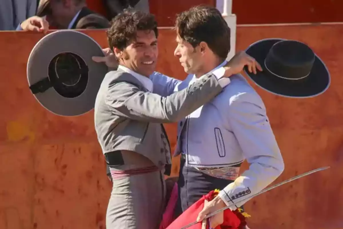 Cayetano Rivera y Canales Rivera vestits amb vestits tradicionals sostenen barrets en una plaça de toros. Cayetano Rivera y Canales Rivera vestits amb vestits tradicionals sostenen barrets en una plaça de toros.