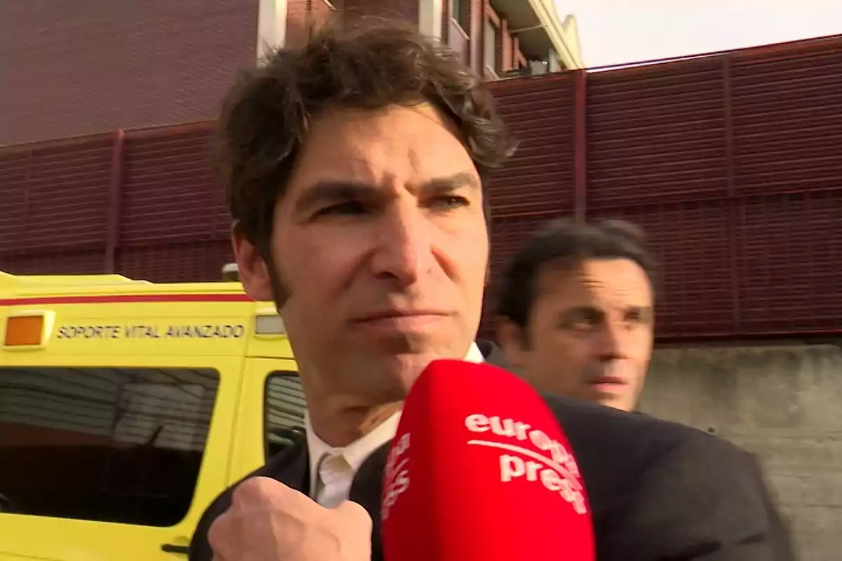Cayetano Rivera amb un micròfon de premsa vermell davant d'una ambulància groga. Cayetano Rivera amb un micròfon de premsa vermell davant d'una ambulància groga.