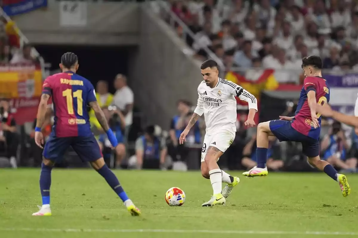 Jugadors de futbol en acció durant un partit, un amb uniforme blanc i altres amb uniforme blau i vermell, en un estadi ple d'espectadors. Jugadors de futbol en acció durant un partit, un amb uniforme blanc i altres amb uniforme blau i vermell, en un estadi ple d'espectadors.