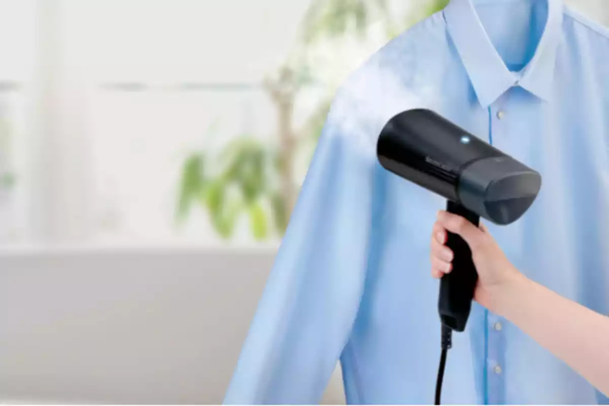 Persona utilitzant un vaporitzador de mà per treure arrugues d’una camisa blava Persona utilitzant un vaporitzador de mà per treure arrugues d’una camisa blava