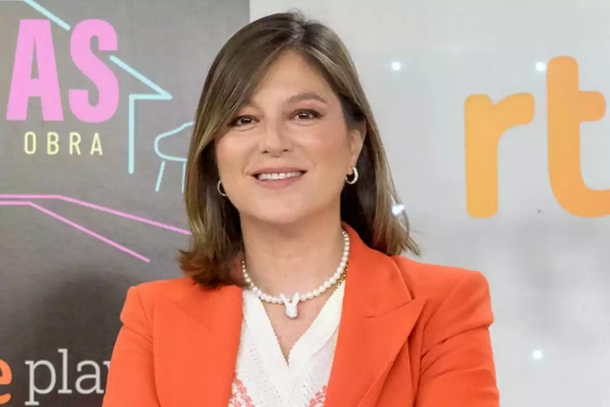 Captura de Chabeli Iglesias somrient amb cabell castany i laci, vestida amb un blazer taronja i un collaret de perles, posa davant d'un fons amb logotips i text colorit a la roda de premsa del seu programa Els Esglésies: Germà a l'obra Captura de Chabeli Iglesias somrient amb cabell castany i laci, vestida amb un blazer taronja i un collaret de perles, posa davant d'un fons amb logotips i text colorit a la roda de premsa del seu programa Els Esglésies: Germà a l'obra