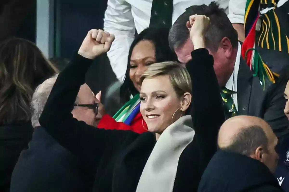 Charlene somrient amb els braços a dalt, jersei negre i bufanda gris Charlene somrient amb els braços a dalt, jersei negre i bufanda gris