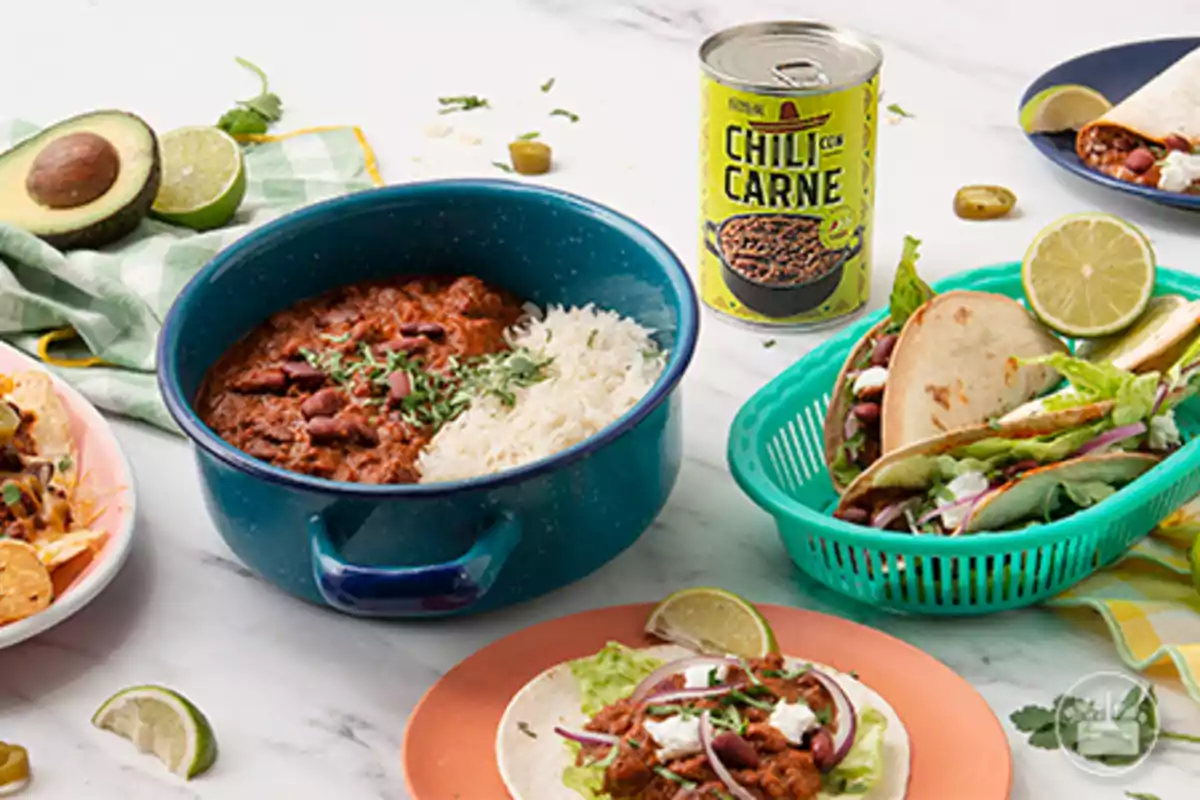 Un plat de chili amb carn acompanyat d'arròs en una olla blava, envoltat de tacos, nachos i un alvocat sobre una taula de marbre. Un plat de chili amb carn acompanyat d'arròs en una olla blava, envoltat de tacos, nachos i un alvocat sobre una taula de marbre.