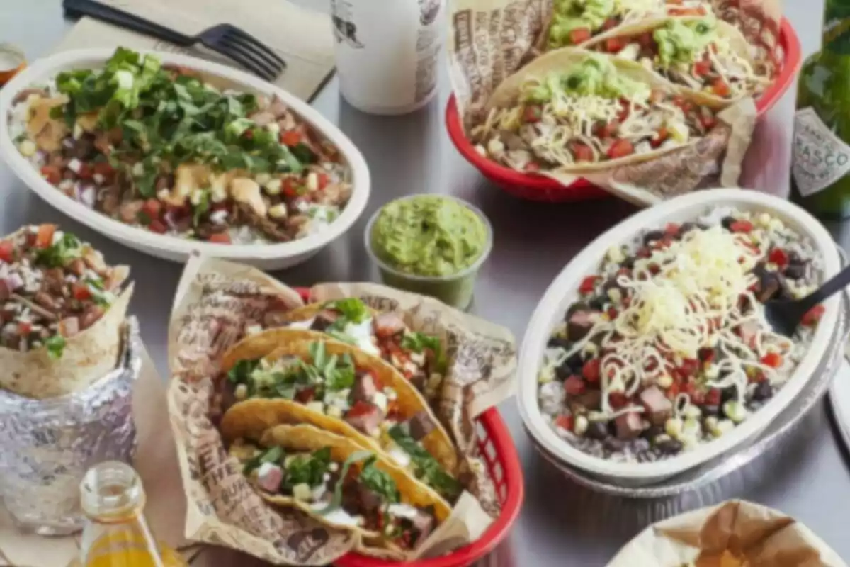 Several Mexican dishes such as burritos, tacos, guacamole, and bowls served on a table alongside drinks and salsa Several Mexican dishes such as burritos, tacos, guacamole, and bowls served on a table alongside drinks and salsa
