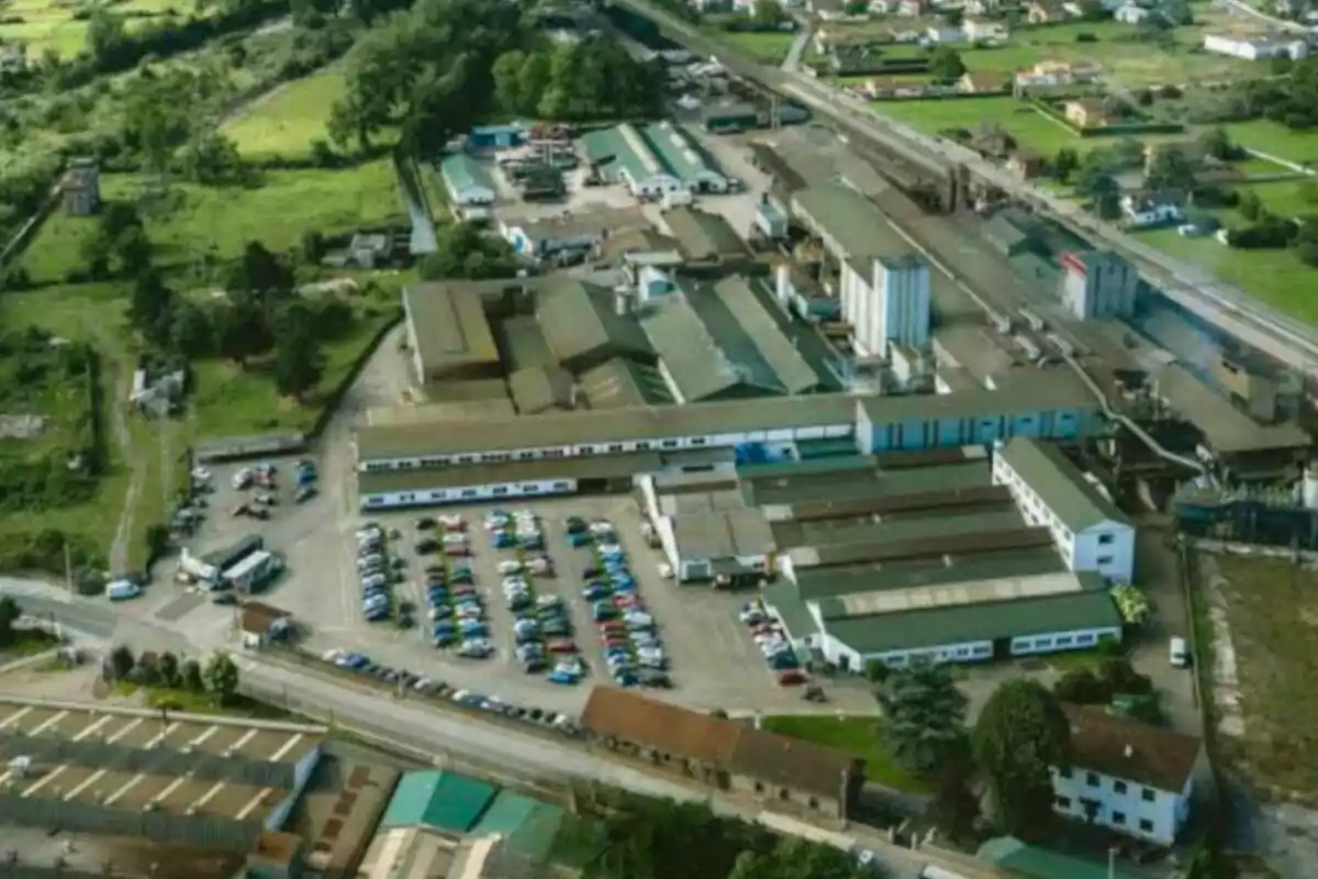 Vista aérea de un complejo industrial con varios edificios, estacionamiento lleno de autos y áreas verdes alrededor