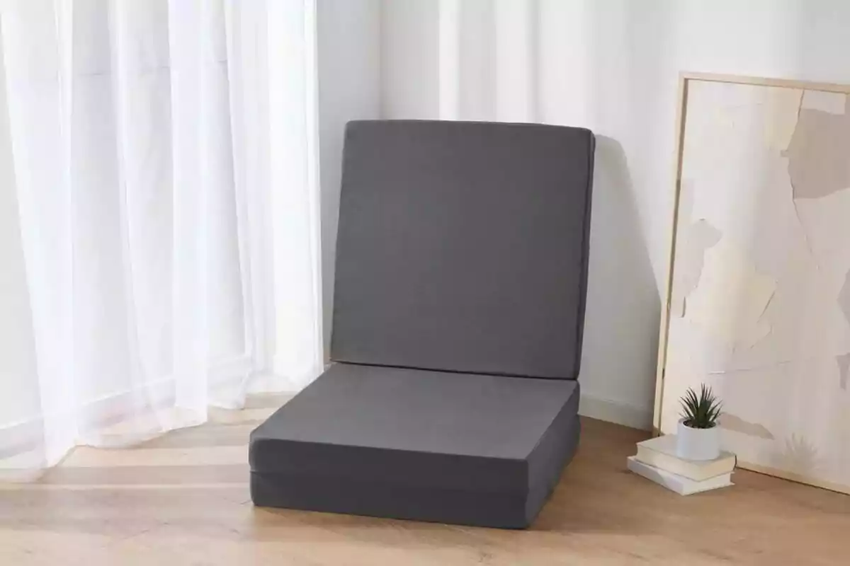 Una cadira plegable grisa en una habitació amb terra de fusta, al costat d'una finestra amb cortines blanques i un quadre recolzat a la paret. Una cadira plegable grisa en una habitació amb terra de fusta, al costat d'una finestra amb cortines blanques i un quadre recolzat a la paret.