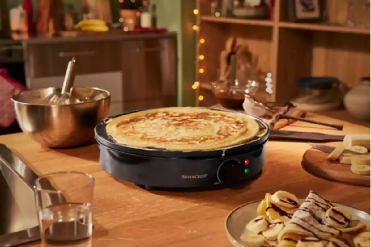 Una crepera eléctrica cocinando un crepe en una cocina acogedora con utensilios y plátanos en la mesa. Una crepera eléctrica cocinando un crepe en una cocina acogedora con utensilios y plátanos en la mesa.