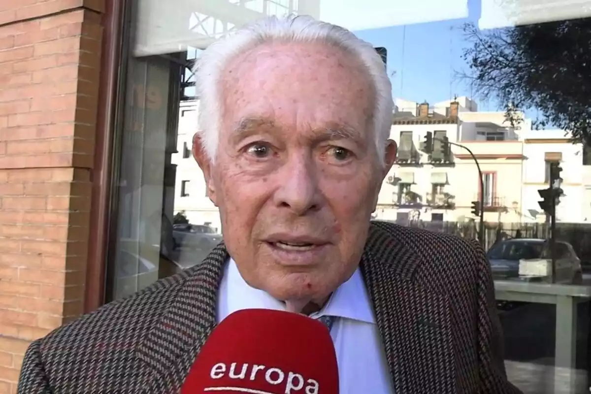 Primer pla de Curro Romero parlant amb un vestit marró davant d'un micròfon vermell Primer pla de Curro Romero parlant amb un vestit marró davant d'un micròfon vermell
