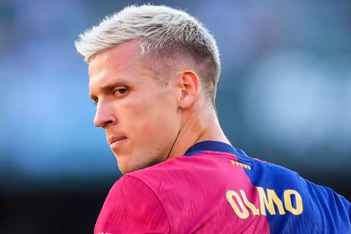 Un jugador de futbol amb cabell ros i samarreta blava i vermella mira cap a un costat.