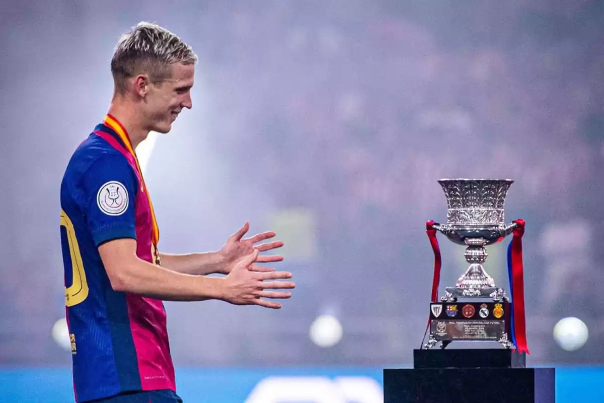 A soccer player with a medal looks at a trophy in a stadium. A soccer player with a medal looks at a trophy in a stadium.