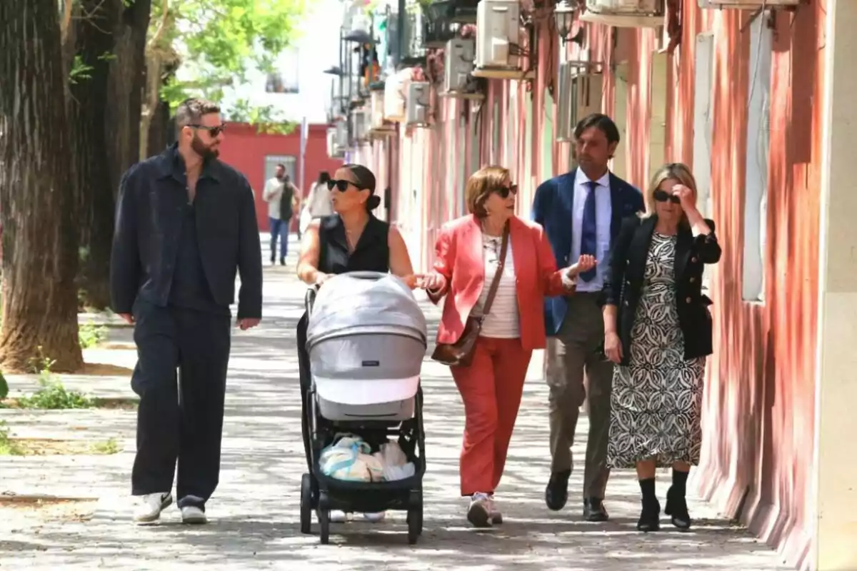 Un grup de persones camina per un carrer arbrat, una d'elles empeny un cotxet de nadó mentre conversen animadament. Un grup de persones camina per un carrer arbrat, una d'elles empeny un cotxet de nadó mentre conversen animadament.