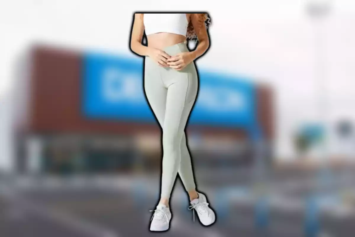 Dona amb top blanc i leggings verds posant davant d'un edifici borrós.