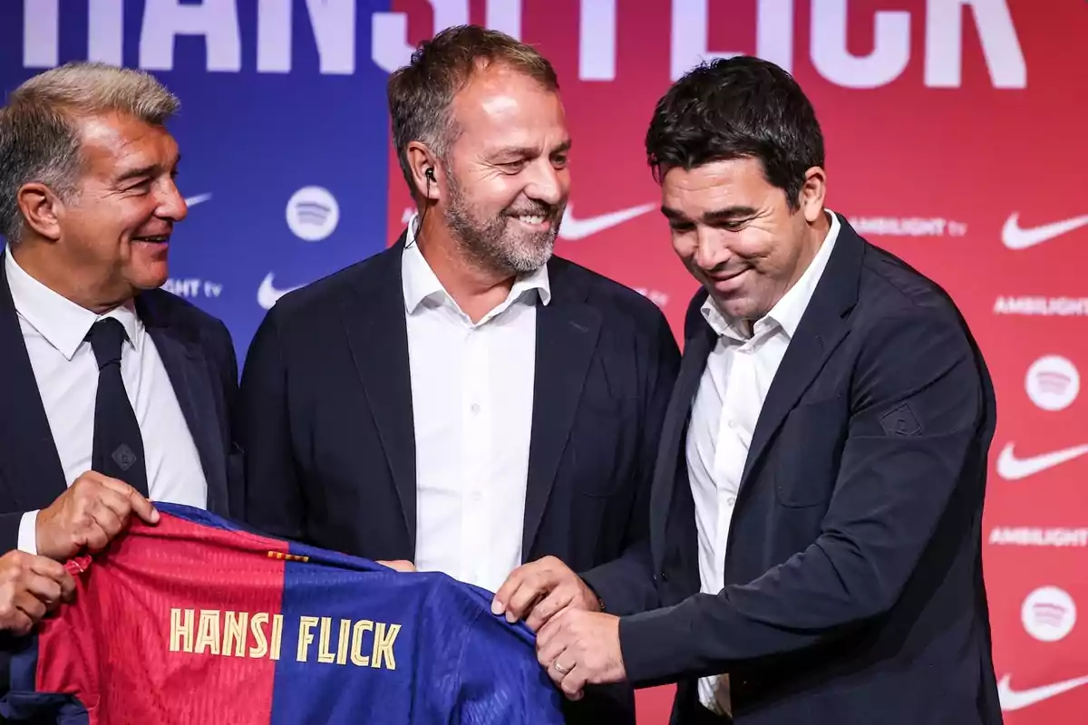Tres homes somriuen mentre sostenen una samarreta de futbol amb el nom Tres homes somriuen mentre sostenen una samarreta de futbol amb el nom