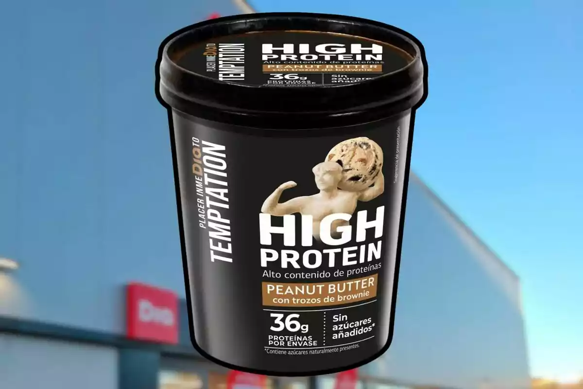 Envàs de gelat alt en proteïnes amb gust de mantega de cacauet i trossos de brownie, amb 36 grams de proteïnes per envàs i sense sucres afegits, sobre un fons de cel blau i edifici. Envàs de gelat alt en proteïnes amb gust de mantega de cacauet i trossos de brownie, amb 36 grams de proteïnes per envàs i sense sucres afegits, sobre un fons de cel blau i edifici.