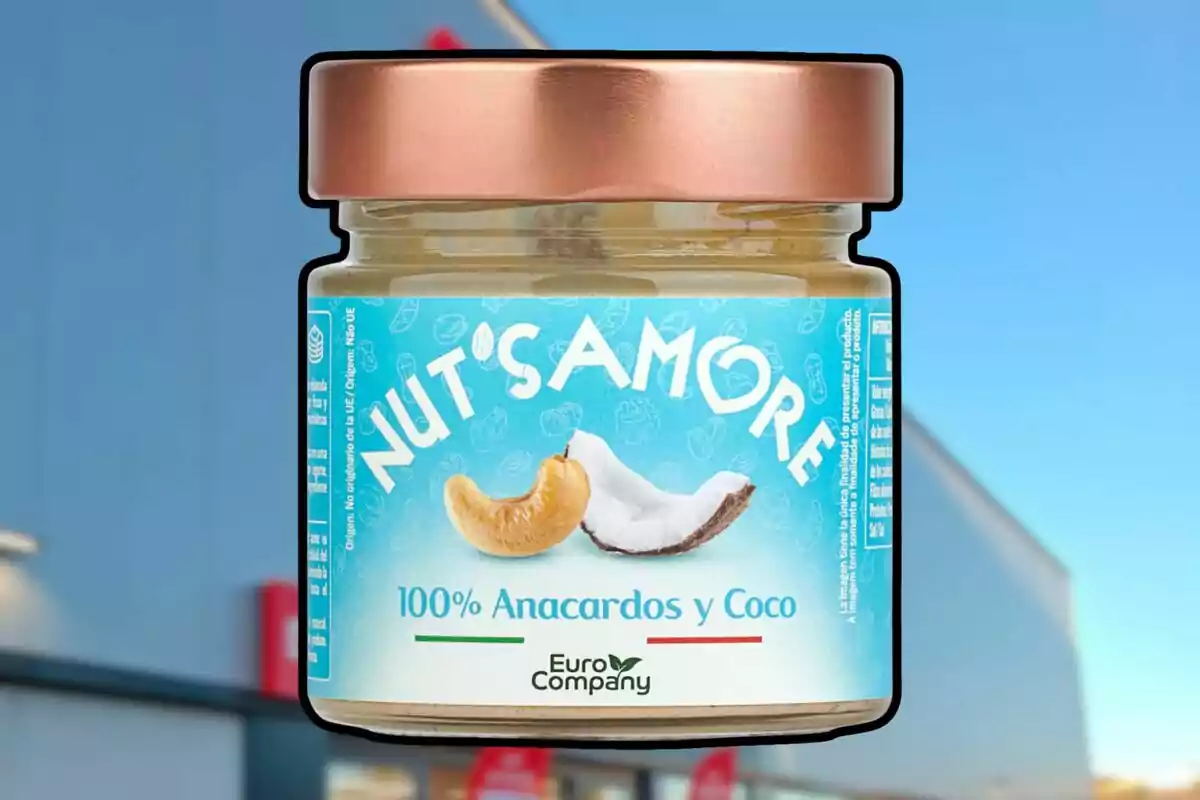 Un pot de vidre amb tapa daurada que conté una crema d'anacards i coco de la marca Nut's Amore, amb un disseny d'etiqueta blau clar que mostra imatges d'anacards i coco. Un pot de vidre amb tapa daurada que conté una crema d'anacards i coco de la marca Nut's Amore, amb un disseny d'etiqueta blau clar que mostra imatges d'anacards i coco.
