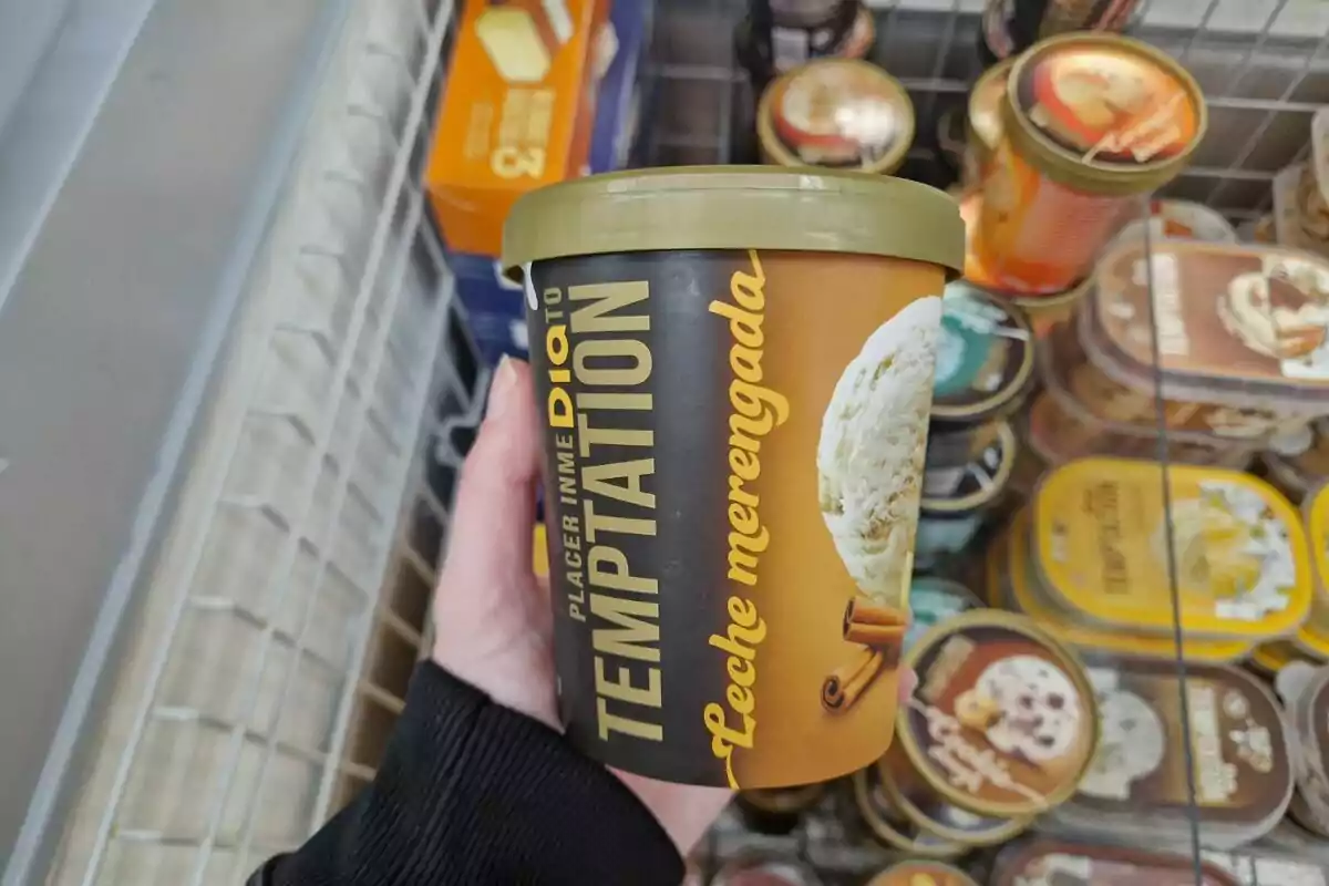 Envàs de gelat de llet merengada amb canyella de la marca Temptation sostingut per una mà en un supermercat. Envàs de gelat de llet merengada amb canyella de la marca Temptation sostingut per una mà en un supermercat.