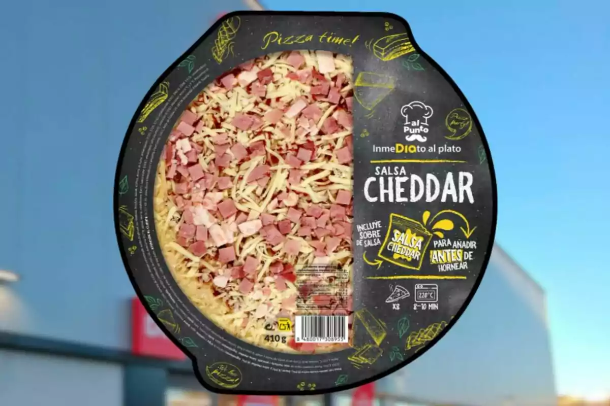 Pizza congelada amb pernil i formatge ratllat en envàs rodó, amb etiqueta que indica que inclou salsa cheddar per afegir abans de coure. Pizza congelada amb pernil i formatge ratllat en envàs rodó, amb etiqueta que indica que inclou salsa cheddar per afegir abans de coure.