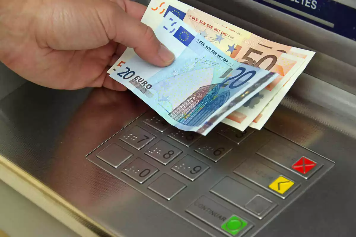 Mà esquerra d'una persona sostenint un bitllet de 20 euros i dos bitllets de 50 euros, en un caixer automàtic