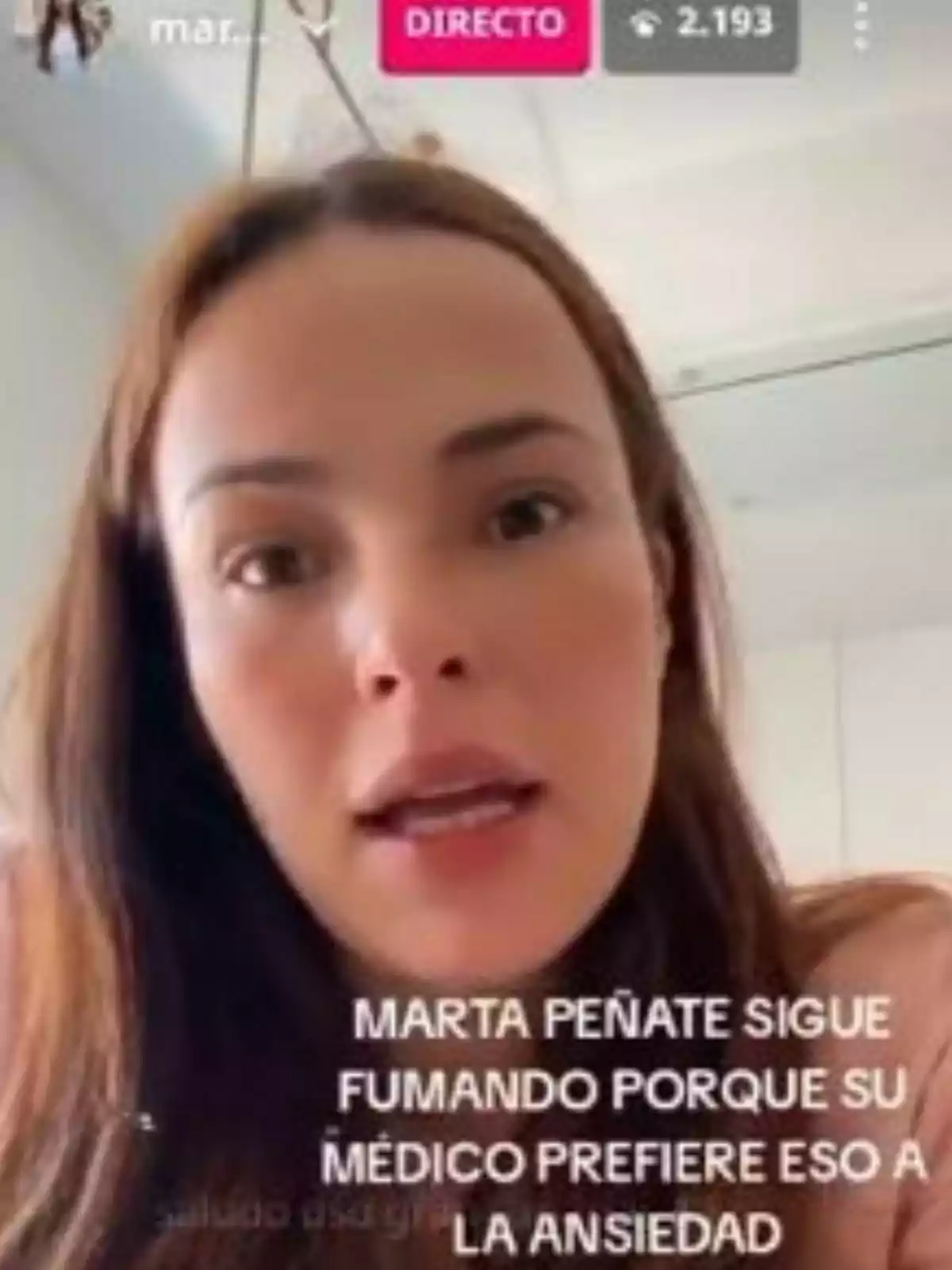Marta Peñate parlant davant de la càmera durant una transmissió en directe amb un text a la pantalla que menciona que continua fumant per recomanació mèdica per controlar l’ansietat. Marta Peñate parlant davant de la càmera durant una transmissió en directe amb un text a la pantalla que menciona que continua fumant per recomanació mèdica per controlar l’ansietat.