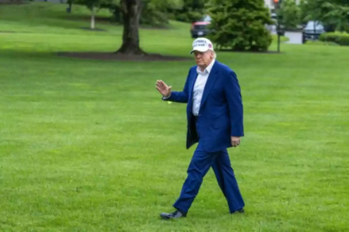 Imatge de Donald Trump vestit amb un vestit blau i una gorra blanca caminant sobre gespa verda i saludant amb la mà. Imatge de Donald Trump vestit amb un vestit blau i una gorra blanca caminant sobre gespa verda i saludant amb la mà.