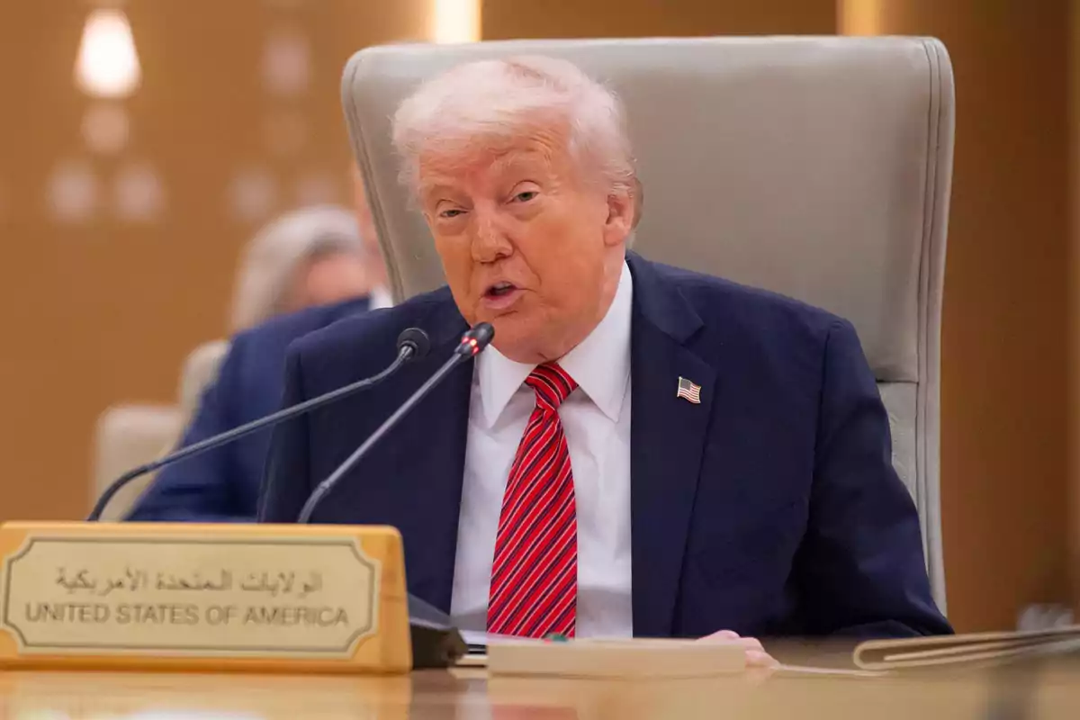 Donald Trump amb vestit fosc i corbata vermella parla en un micròfon durant una conferència, amb un cartell que diu Donald Trump amb vestit fosc i corbata vermella parla en un micròfon durant una conferència, amb un cartell que diu