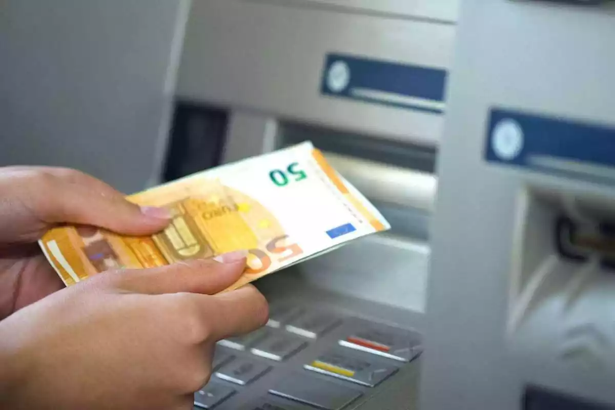 Dos mans d'una persona sostenint bitllets de 50 euros davant d'un caixer automàtic