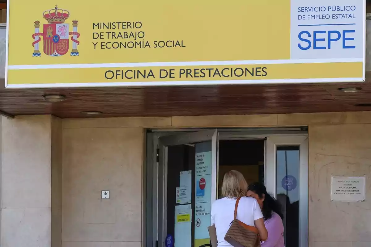 Dues persones conversant davant de l'entrada d'una oficina de prestacions del Ministeri de Treball i Economia Social d'Espanya.