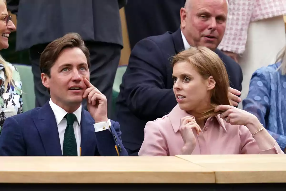 Edoardo Mapelli i Beatriz de York asseguts en un esdeveniment esportiu, envoltats d'altres persones, amb expressions d'interès i conversa. Edoardo Mapelli i Beatriz de York asseguts en un esdeveniment esportiu, envoltats d'altres persones, amb expressions d'interès i conversa.