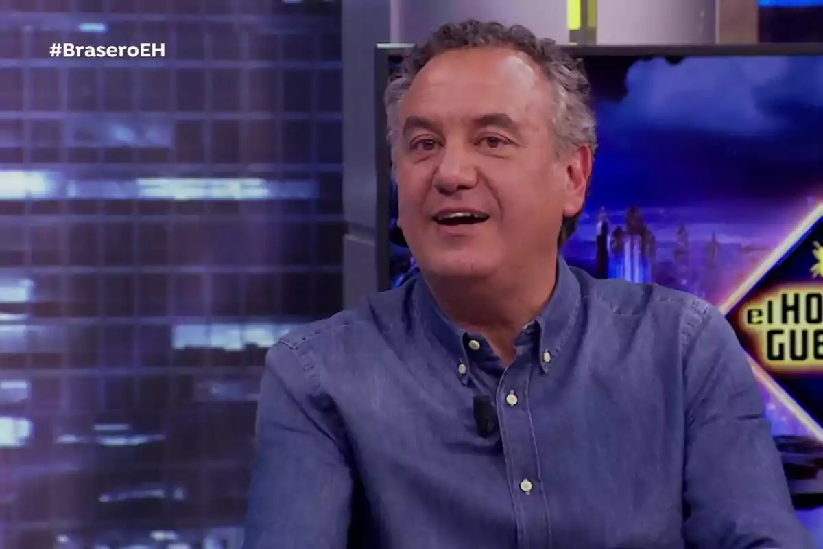Roberto Brasero amb camisa de mezclilla somriu mentre està assegut al set de televisió amb el logotip de Roberto Brasero amb camisa de mezclilla somriu mentre està assegut al set de televisió amb el logotip de