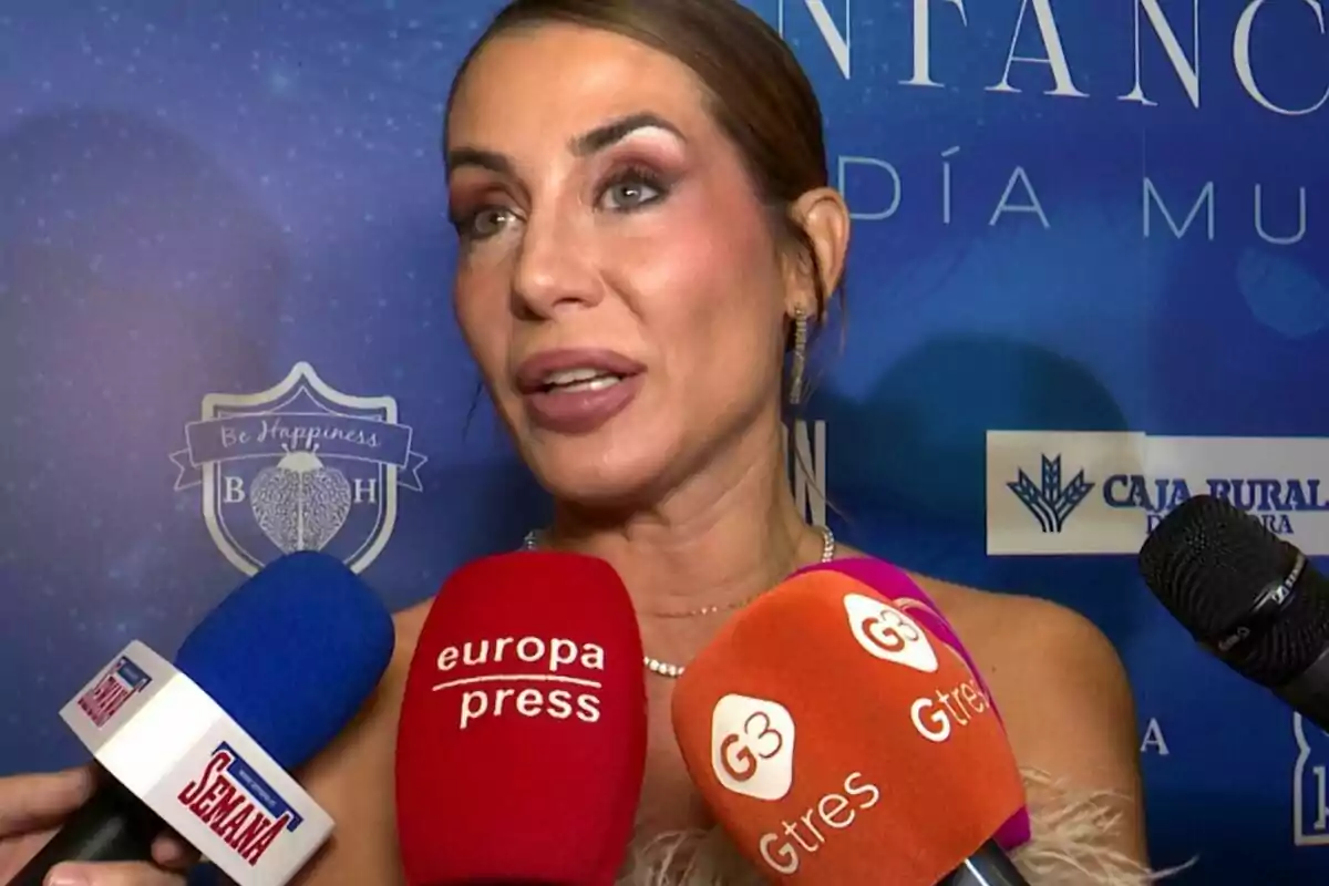Elena Tablada sent entrevistada per diversos mitjans de comunicació amb micròfons de diferents colors davant d'un fons blau amb logotips. Elena Tablada sent entrevistada per diversos mitjans de comunicació amb micròfons de diferents colors davant d'un fons blau amb logotips.