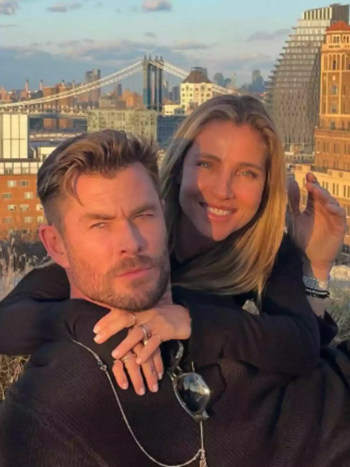 Elsa Pataky i Chris Hemsworth abraçats i somrients a l’aire lliure amb un pont i edificis de ciutat al fons. Elsa Pataky i Chris Hemsworth abraçats i somrients a l’aire lliure amb un pont i edificis de ciutat al fons.