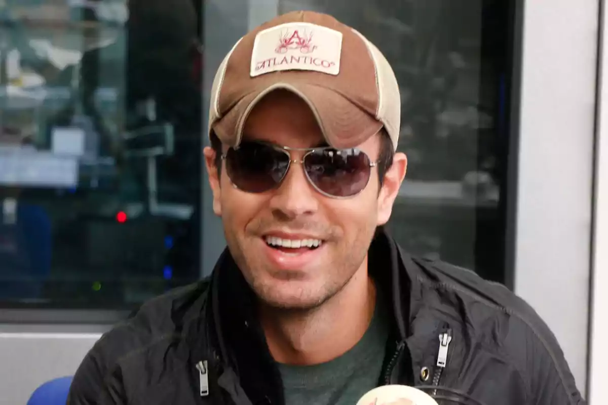 Enrique Iglesias amb gorra i ulleres de sol somriu mentre sosté un micròfon. Enrique Iglesias amb gorra i ulleres de sol somriu mentre sosté un micròfon.