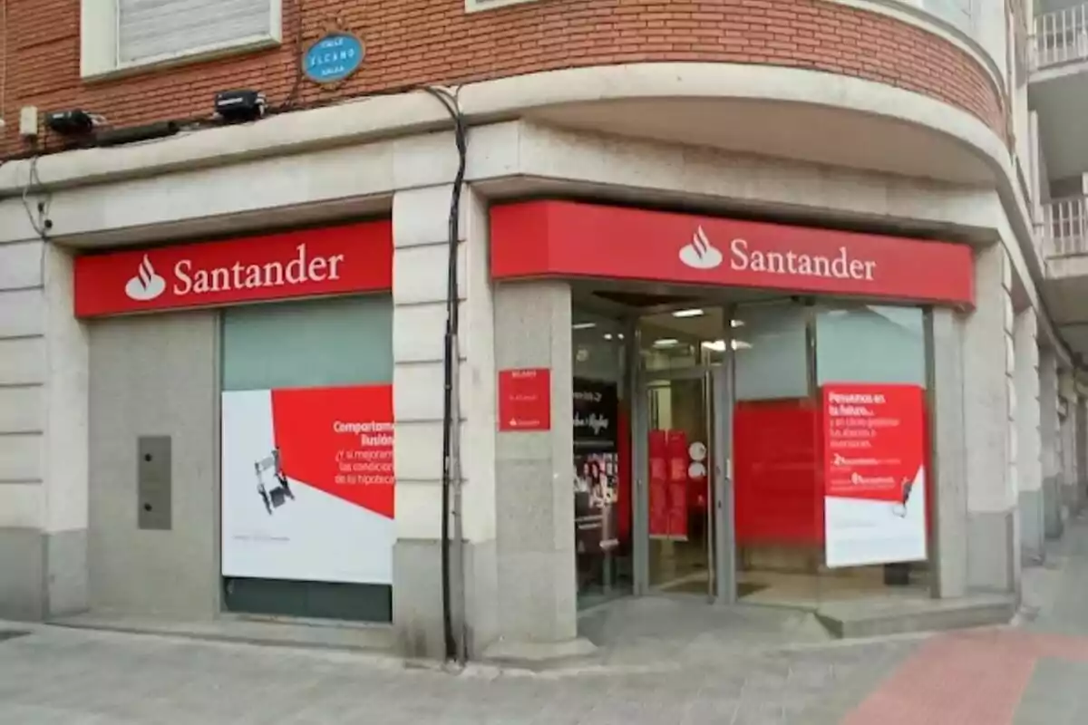 Fachada de una sucursal del banco Santander en una esquina de un edificio de ladrillo con carteles rojos y blancos.