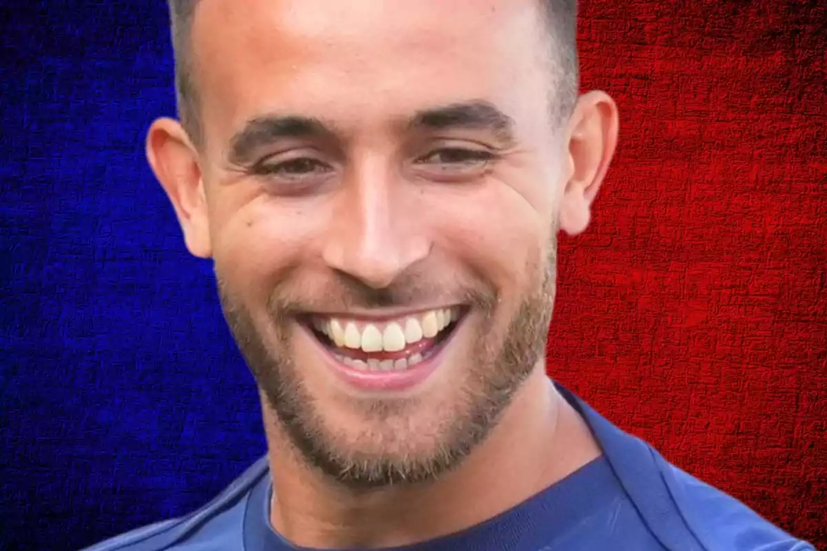 A smiling man with a beard and short hair in front of a blue and red divided background.