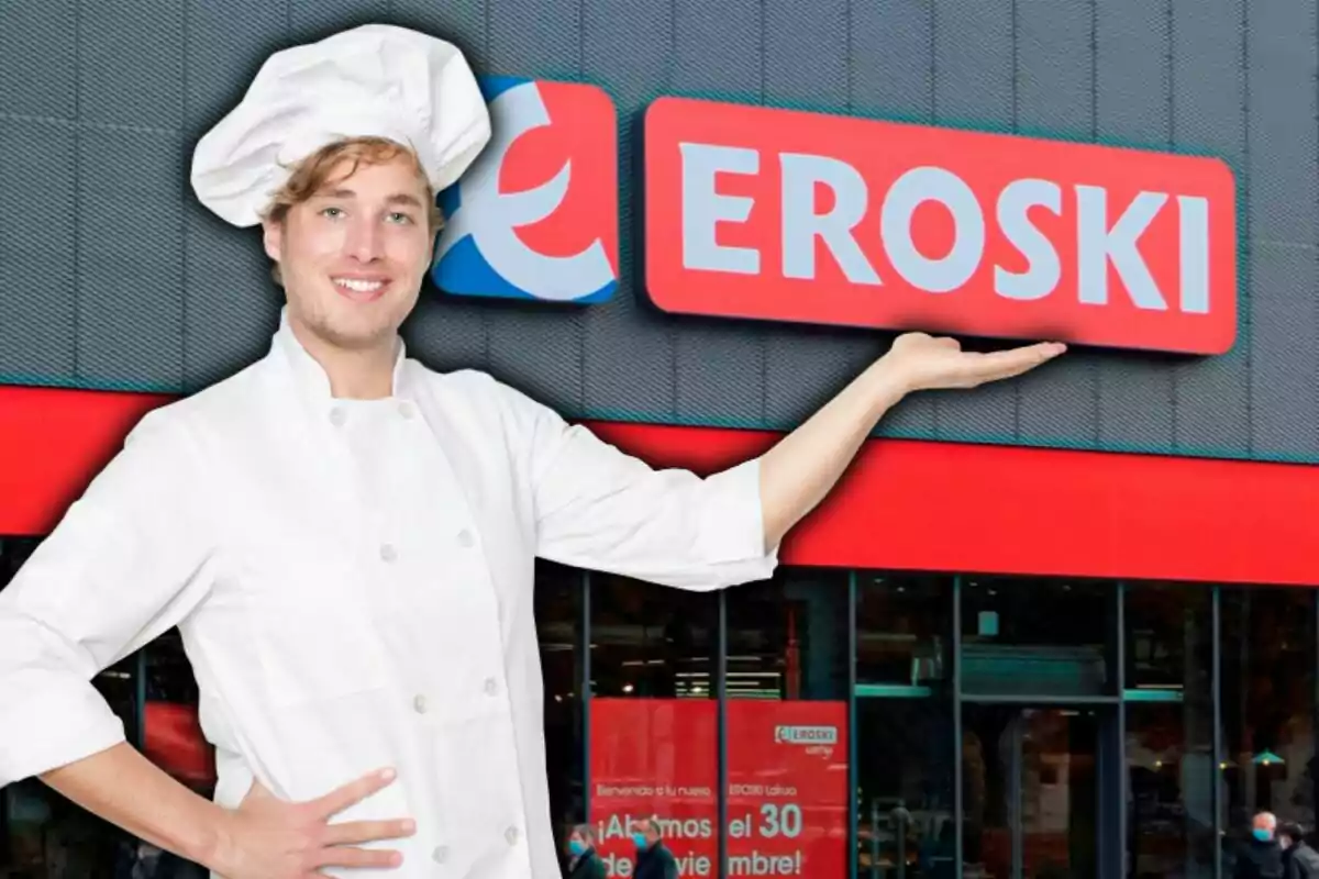 Un xef somrient amb uniforme blanc i gorra de cuiner està davant d'una botiga Eroski, assenyalant el rètol amb una mà.